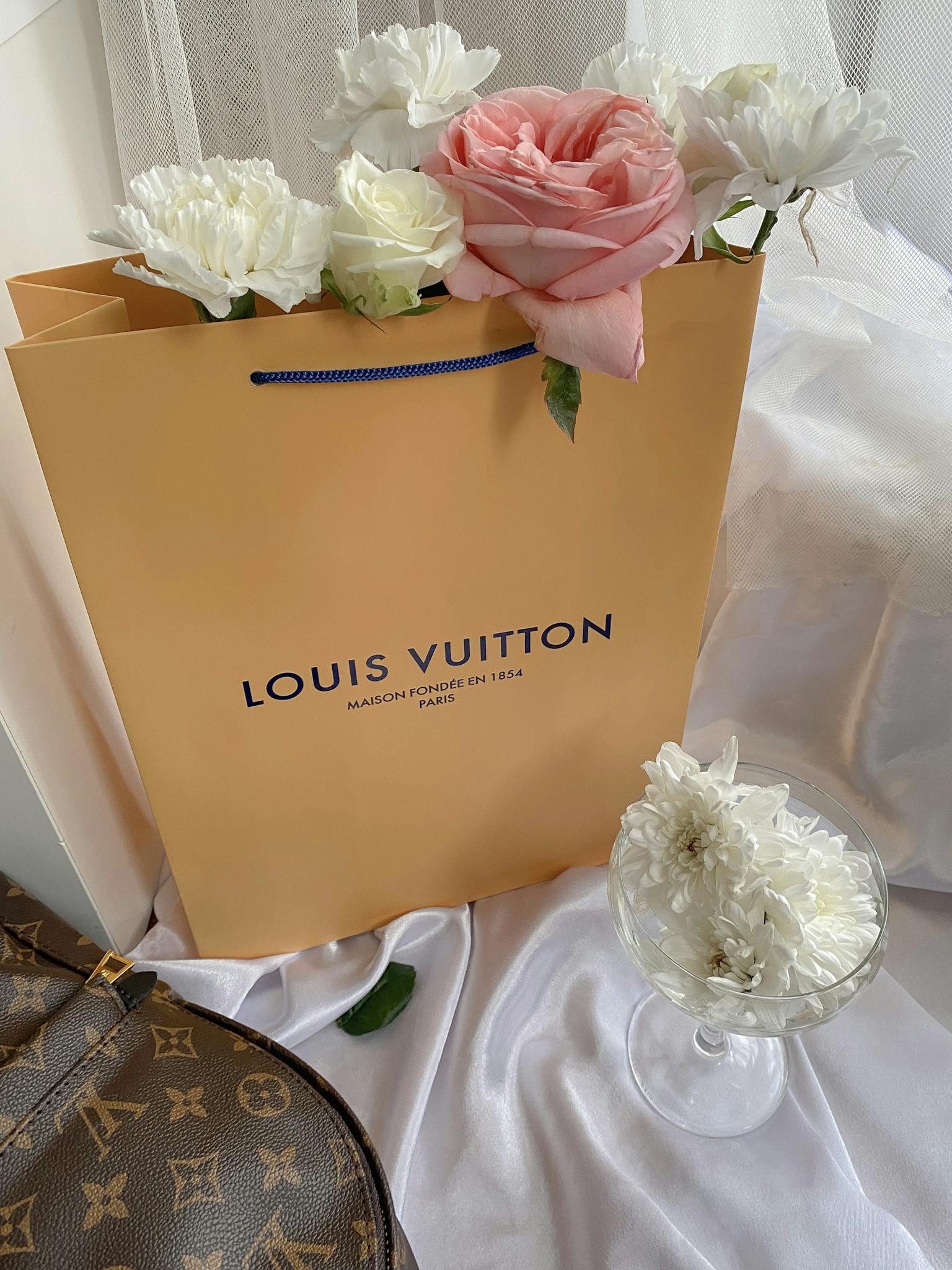 A Louis Vuitton paper bag with elegant fresh flowers for a luxurious still life scene.