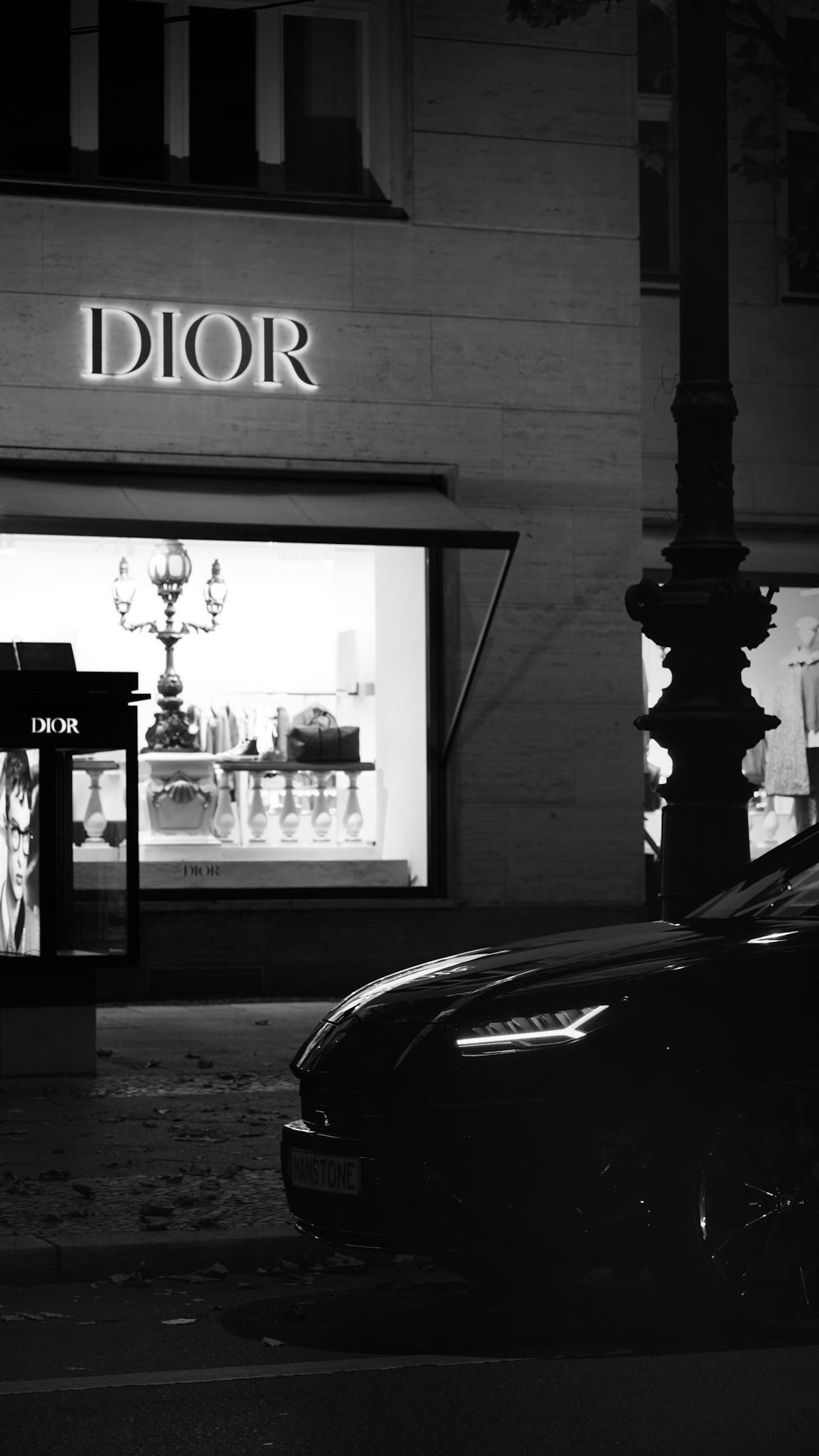 Elegant black and white photo of a Dior boutique in Berlin at night, featuring a luxury car.